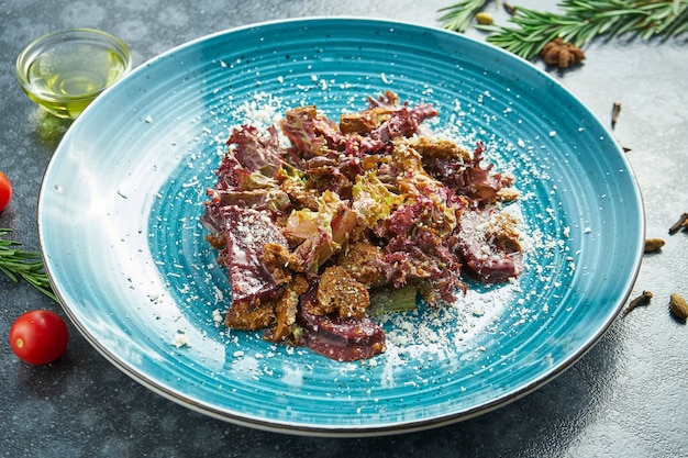 Insalata appetitosa con arrosto di manzo, lattuga e foglie di parmigiano su un piatto blu su una superficie nera