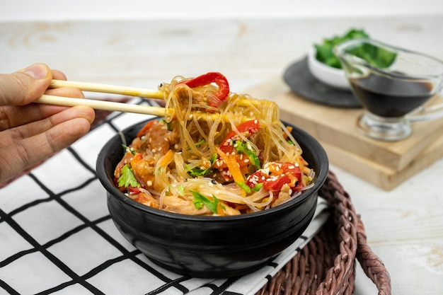 Insalata asiatica con spaghetti di riso, verdure, funghi, pollo e salsa di soia. Funchose con pasta bianca trasparente in banda nera
