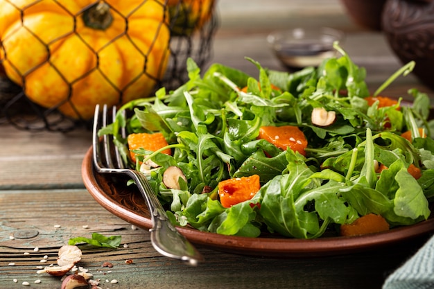 Insalata autunnale con rucola zucca al forno nocciola e semi di sesamo su piatto marrone Dieta Paleo