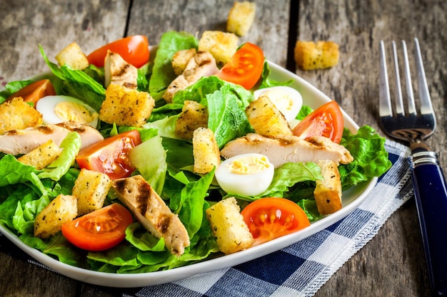 Insalata Caesar con crostini, uova di quaglia, pomodorini e pollo alla griglia su tavola rustica