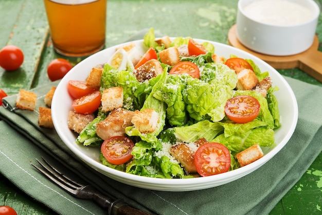 Insalata Caesar con filetto di pollo, pomodori, crostini e parmigiano in un piatto su fondo rustico in legno, primo piano