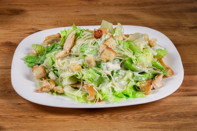 Insalata caesar fresca con pezzi di pollo servita su piatto bianco su fondo di legno