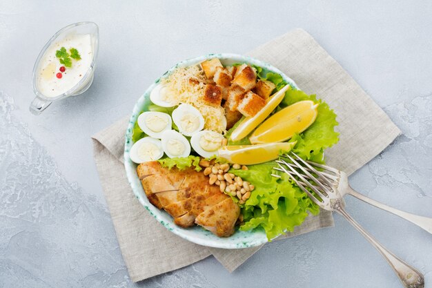 Insalata Caesar tradizionale con uova di quaglia e pinoli in una ciotola di ceramica leggera Su una superficie di pietra grigia o cemento. Ciotola per il pranzo. Messa a fuoco selettiva. Vista dall'alto.