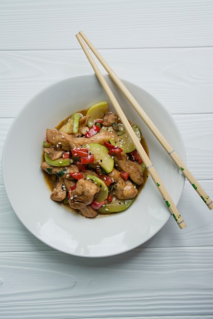 Insalata calda con pollo, zucchine e peperoncino, cosparsa di semi di sesamo ed erbe. Cibo asiatico. Legno bianco .