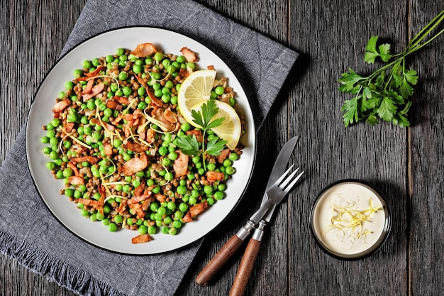 Insalata calda libanese di lenticchie e piselli con pancetta scorza di limone e salsa di limone e olio d'oliva servita su un piatto su uno sfondo di legno scuro vista dall'alto primo piano