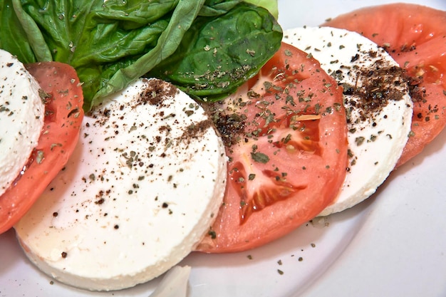 Insalata caprese con pomodoro, basilico, mozzarella, formaggio fresco, spinaci e cibo spolverato di pepe nero