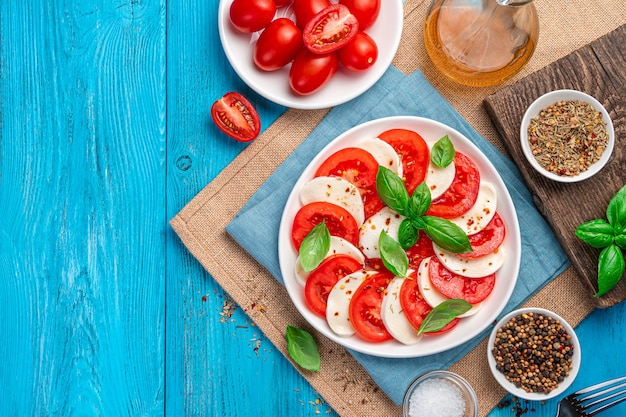 Insalata caprese di pomodori freschi tritati, mozzarella, basilico e olio d'oliva su un tavolo di legno blu. Cucina tradizionale italiana