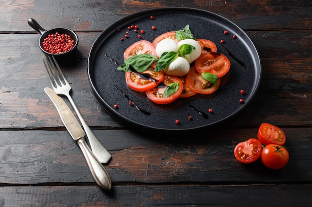 Insalata caprese Fette di pomodoro e mozzarella con foglie di basilico su tavola scura in legno d'ulivo.