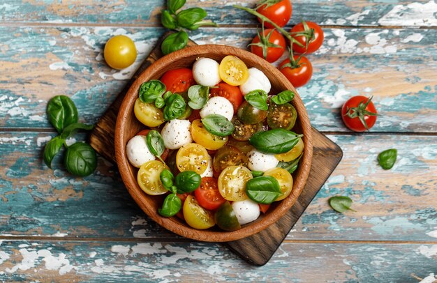 Insalata caprese italiana con pomodori a fette, mozzarella, basilico, olio d'oliva in una ciotola di legno.