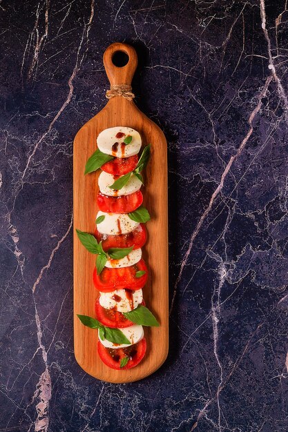Insalata caprese italiana con pomodori a fette, mozzarella, basilico, olio d'oliva su un tagliere di legno.