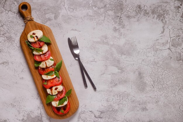 Insalata caprese italiana con pomodori a fette mozzarella basilico olio d'oliva su un tagliere di legno