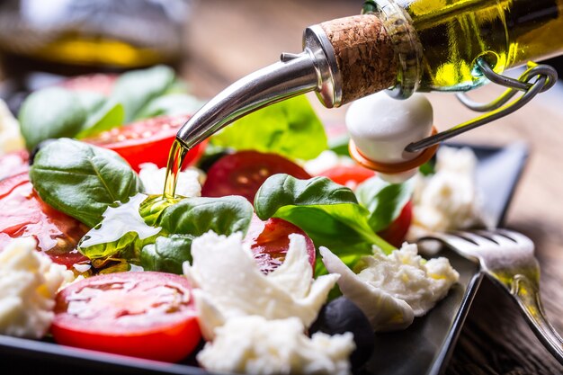 Insalata caprese Mozzarella pomodorini basilico e olio d'oliva su tavola di quercia antica Cucina italiana