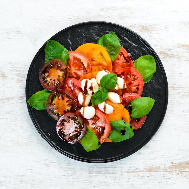 Insalata caprese su un piatto nero. Pomodori, mozzarella e basilico. Vista dall'alto. Spazio libero per il tuo testo.