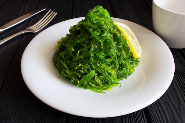 Insalata con alghe e sesamo nel piatto bianco sul legno nero