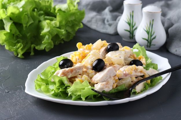 Insalata con ananas, pollo al forno, mais e olive nere sul piatto bianco