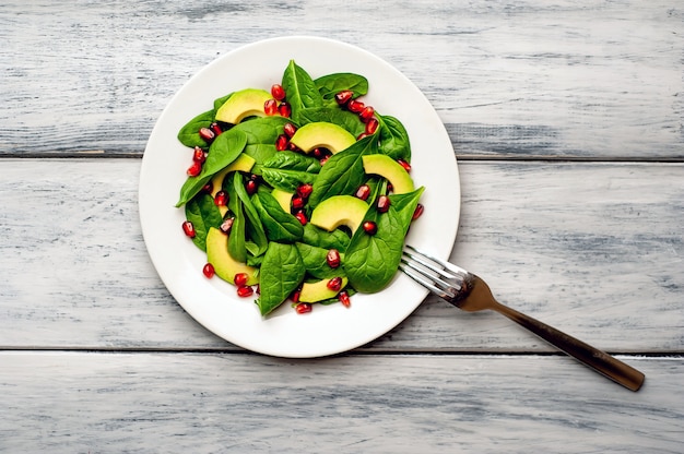 insalata con avocado, rucola, spinaci, melograno, semi su fondo di legno