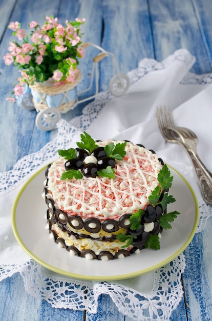 Insalata con bastoncini di granchio, formaggio, uova e prugne. Decorato con fiori di olive