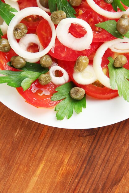 Insalata con capperi nel piatto sul primo piano di legno del fondo