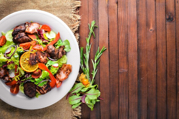 Insalata con cetrioli freschi, pomodori e verdure con carne alla griglia su un piatto Tavola di legno. Vista dall'alto. Spazio libero.