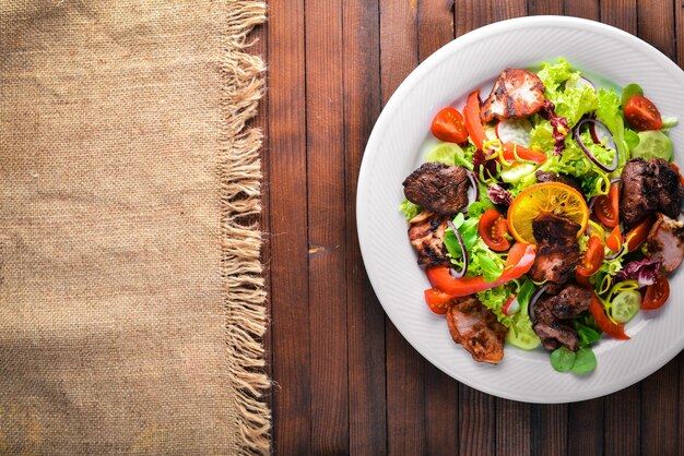 Insalata con cetrioli freschi pomodori e verdure con carne alla griglia su un piatto Tavola di legno Vista dall'alto Spazio libero