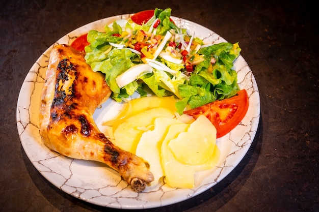 Insalata con coscia di pollo e insalata su fondo nero, su piatto bianco