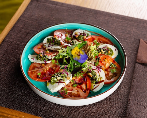 Insalata con fette di formaggio succosi pomodori guarniti con microgreens al pesto