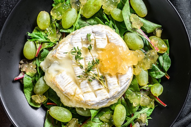 Insalata con formaggio Camembert al forno, uva, bietole e rucola. Sfondo nero. Vista dall'alto.