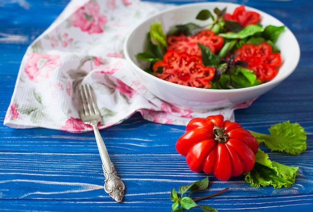 Insalata con il grande pomodoro rosso maturo con basilico su una tavola di legno blu