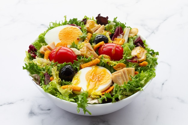 Insalata con lattuga uova tonno olive e miele e vinaigrette di senape su sfondo bianco