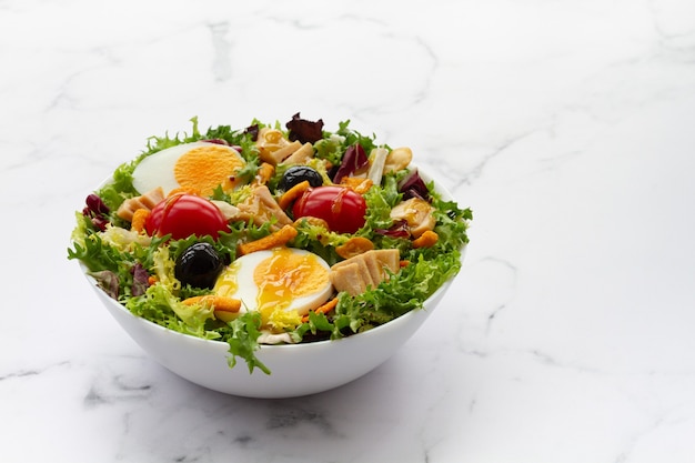 Insalata con lattuga uova tonno olive e miele e vinaigrette di senape su sfondo bianco