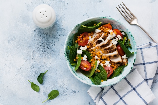 Insalata con lenticchie rosse, foglie di spinaci, pomodorini, carne di pollo e mozzarella in piatto di ceramica sulla vecchia superficie grigia di cemento.