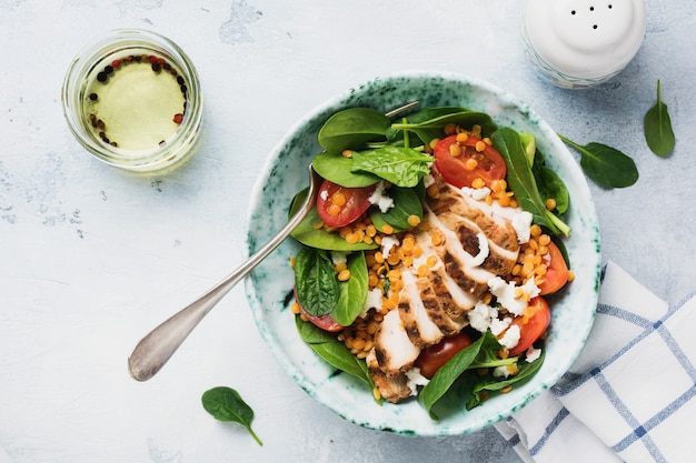 Insalata con lenticchie rosse, foglie di spinaci, pomodorini, carne di pollo e mozzarella in piatto di ceramica sulla vecchia superficie grigia di cemento.