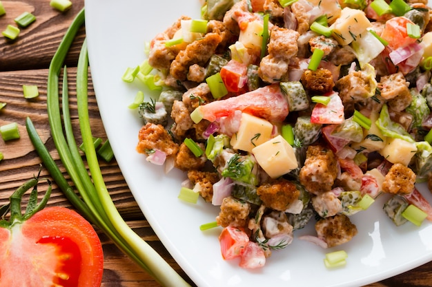 Insalata con maionese vicino alle cipolle verdi e alla metà di un pomodoro su una tavola di legno