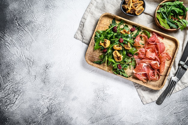 Insalata con Parma, prosciutto crudo, rucola e fichi. Antipasti italiani. Sfondo grigio, vista dall'alto, spazio per il testo