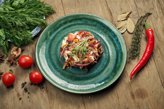 Insalata con pomodori, funghi in scatola, cipolle e manzo bollito su un piatto blu su un tavolo di legno. Medina di insalata slava. Avvicinamento