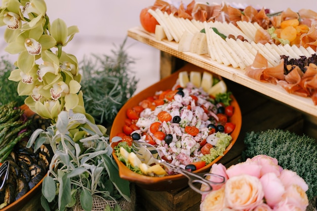 Insalata con pomodoro e olive nere in un piatto e tavola di formaggio e prosciutto su un tavolo con