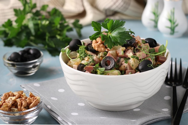 Insalata con prosciutto, ananas, olive nere e noci in una ciotola bianca su fondo azzurro