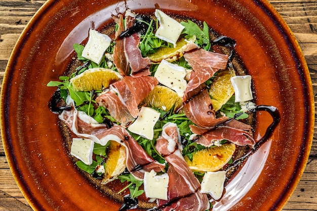 Insalata con prosciutto di Parma, parmigiano, rucola e mandarino su un piatto.