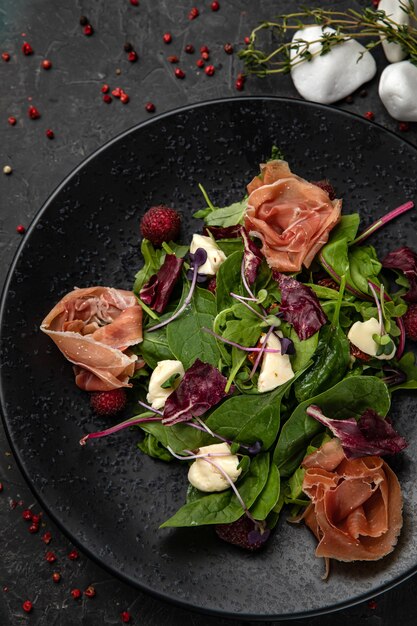 Insalata con prosciutto, erbe aromatiche, lamponi, microgreens su un tavolo di cemento scuro