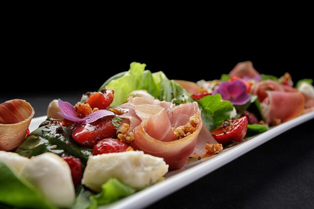 Insalata con prosciutto, fragole e mozzarella su fondo scuro