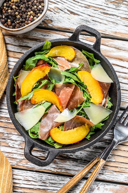 Insalata con prosciutto iberico, rucola, pesca e parmigiano in una padella di ferro