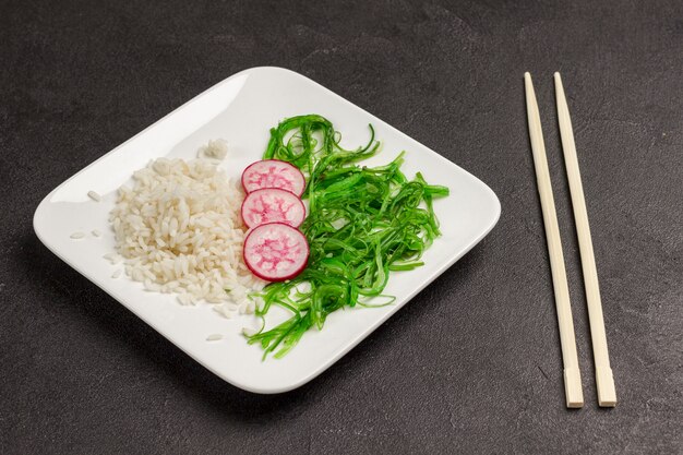 Insalata con riso, ravanello e alghe nel piatto bianco. Cibo asiatico. Bacchette di bambù