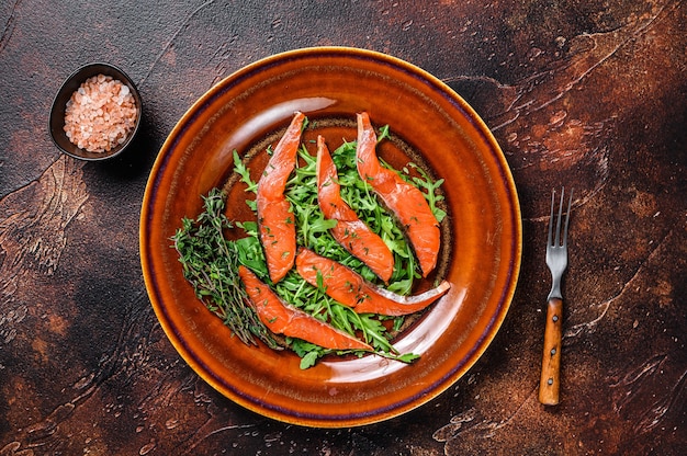 Insalata con rucola e fettine di filetto di salmone affumicato. Sfondo scuro. Vista dall'alto.