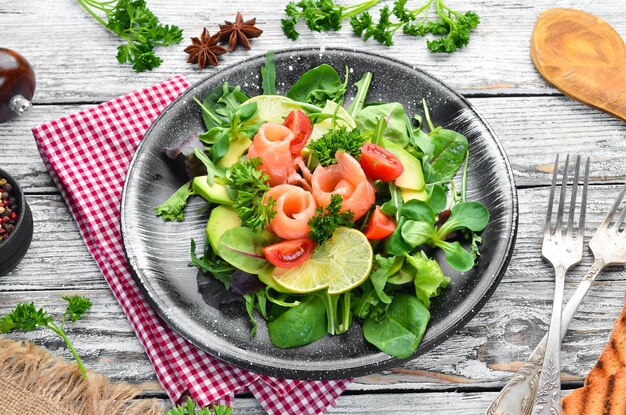 Insalata con salmone, avocado, pomodori e spinaci In un piatto nero su sfondo di legno Vista dall'alto Spazio libero per il testo Disposizione piatta