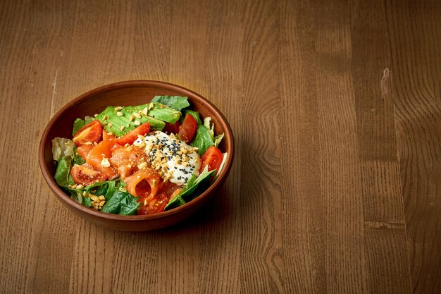 Insalata con salmone leggermente salato e uovo in camicia in un piatto su fondo di legno