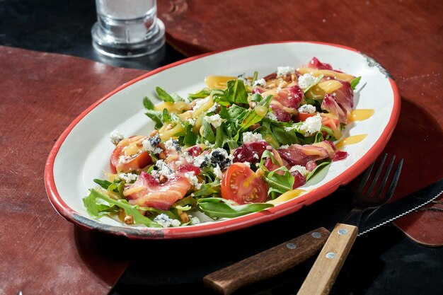 Insalata con salmone leggermente salato, formaggio dorblu, pomodorini e salsa gialla in un piatto bianco. Superficie scura. Luce forte