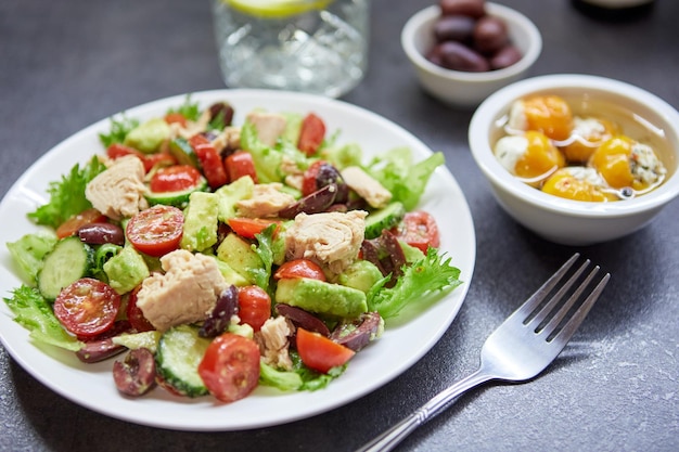 Insalata con tonno lattuga cetrioli pomodori olive e avocado in piatto bianco sul tavolo