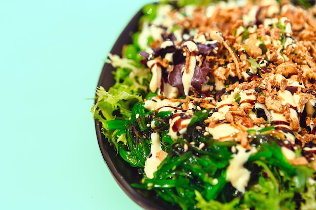 Insalata croccante deliziosa con alga di wakame, cipolla fritta e salsa su un piatto con il fondo della menta