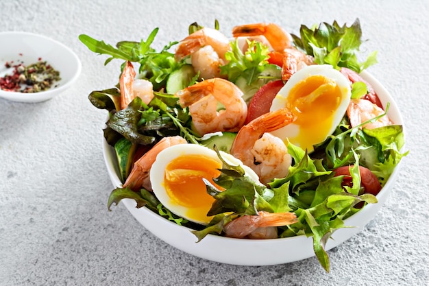 Insalata croccante fresca con verdure e gamberetti di mare in un piatto bianco su sfondo chiaro