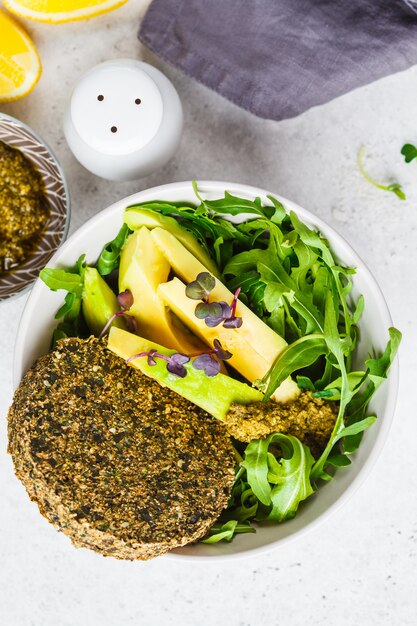 Insalata di avocado verde con cotoletta vegana verde, rucola e pesto in ciotola grigia. Concetto di cibo sano vegano.